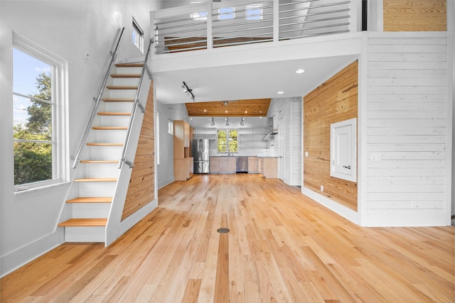 interior space with light hardwood / wood-style flooring, a high ceiling, wooden walls, and a healthy amount of sunlight