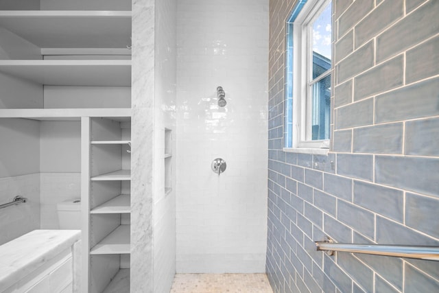 bathroom with tiled shower, toilet, and tile walls