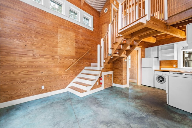 stairway featuring washer / clothes dryer, concrete floors, wood walls, and high vaulted ceiling