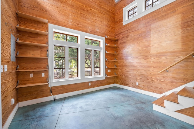 unfurnished room with a towering ceiling, concrete floors, and wood walls