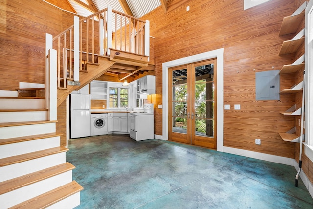 foyer entrance featuring washer / dryer, sink, electric panel, a towering ceiling, and wooden walls