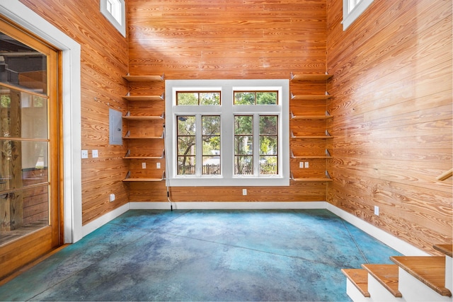 unfurnished room featuring a towering ceiling, a healthy amount of sunlight, and wood walls