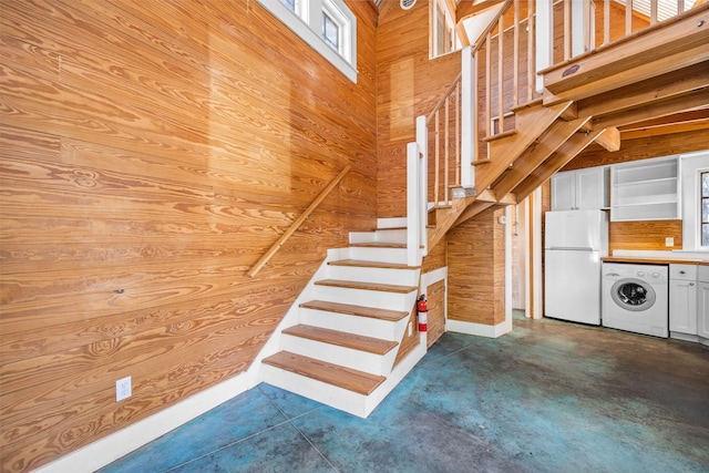 stairs with washer / clothes dryer, concrete floors, wood walls, and a towering ceiling