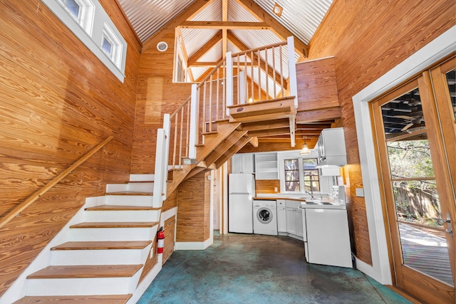 stairs with concrete floors, a healthy amount of sunlight, washer / dryer, and high vaulted ceiling