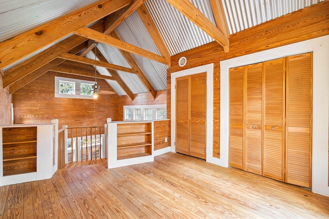 additional living space featuring light hardwood / wood-style flooring, wood walls, and lofted ceiling with beams