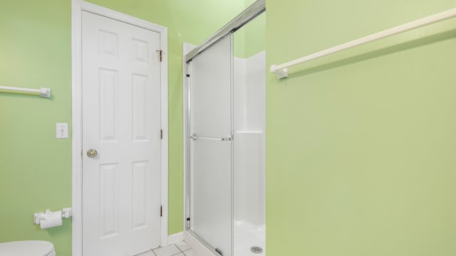 bathroom featuring toilet, a shower with door, and tile patterned floors