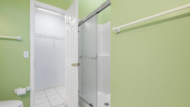 bathroom featuring toilet, a shower with door, and tile patterned floors