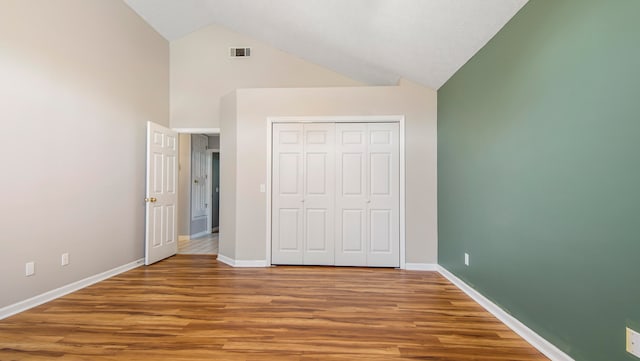 unfurnished bedroom with high vaulted ceiling, wood-type flooring, and a closet