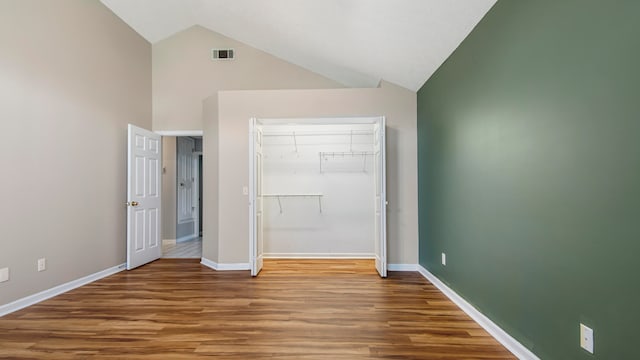 unfurnished bedroom featuring a closet, high vaulted ceiling, and hardwood / wood-style floors