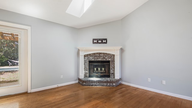 unfurnished living room with hardwood / wood-style flooring, plenty of natural light, a brick fireplace, and lofted ceiling with skylight