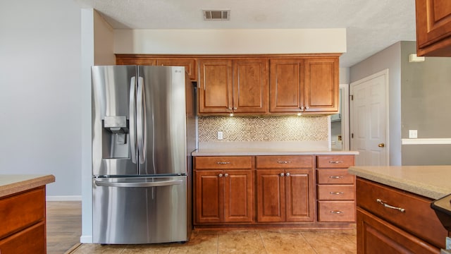 kitchen featuring backsplash, light tile patterned floors, a textured ceiling, and stainless steel refrigerator with ice dispenser