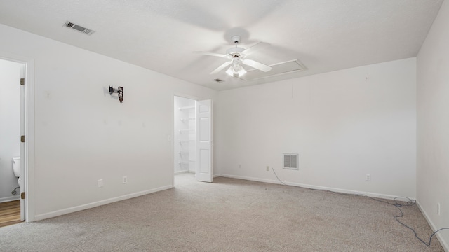 unfurnished bedroom with light colored carpet, ensuite bath, a walk in closet, and ceiling fan