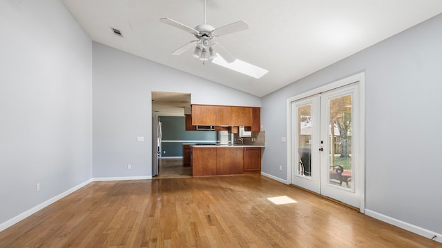 kitchen with kitchen peninsula, hardwood / wood-style flooring, vaulted ceiling with skylight, and ceiling fan