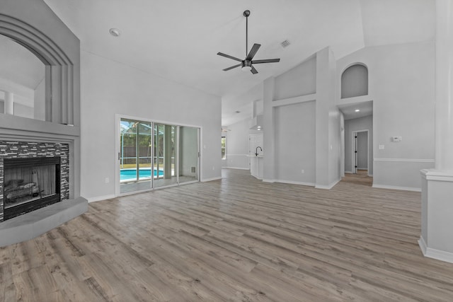 unfurnished living room featuring ceiling fan, light wood-type flooring, a tiled fireplace, and high vaulted ceiling