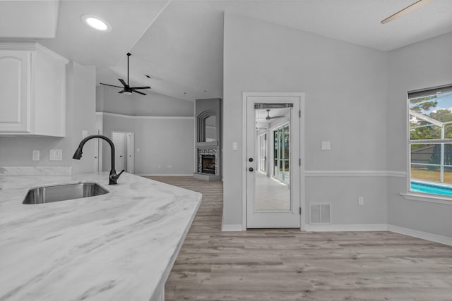 kitchen with light wood-type flooring, white cabinetry, light stone counters, sink, and ceiling fan