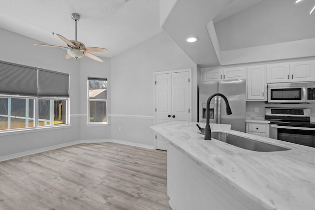 kitchen featuring light wood-type flooring, stainless steel appliances, light stone counters, sink, and white cabinets