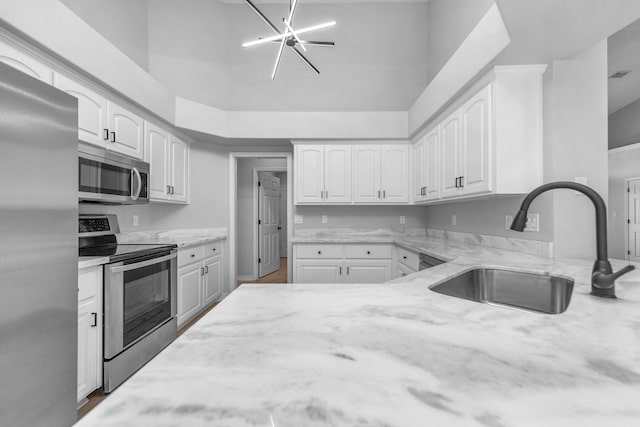 kitchen with stainless steel appliances, light stone counters, sink, and white cabinetry