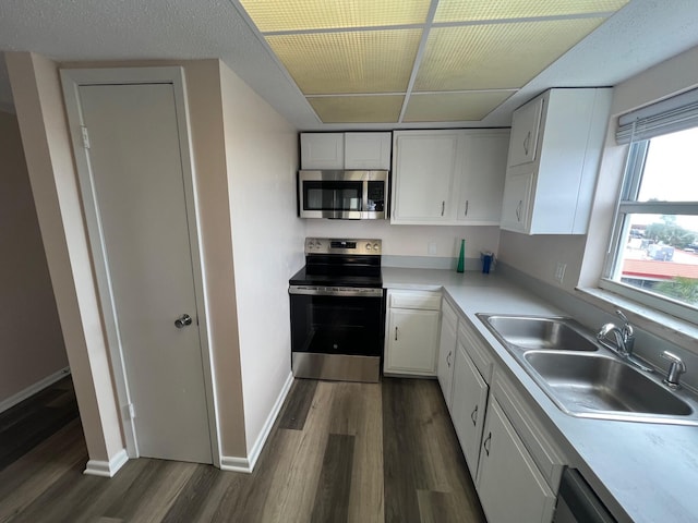 kitchen featuring stainless steel appliances, dark wood-style flooring, a sink, white cabinetry, and light countertops