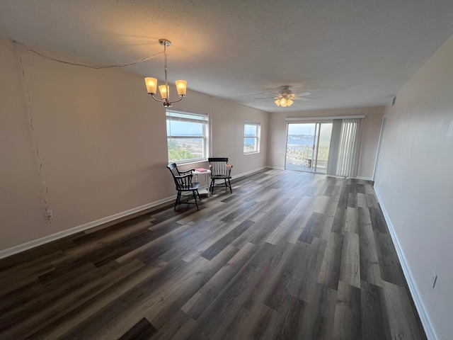 unfurnished dining area with a textured ceiling, ceiling fan with notable chandelier, wood finished floors, and baseboards