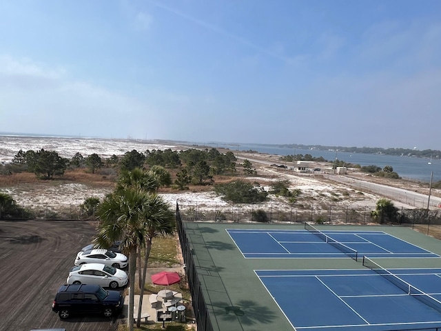 view of tennis court with a water view and fence