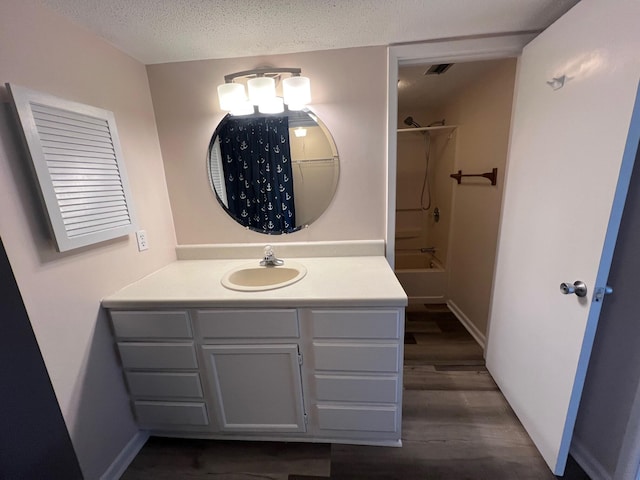 bathroom with a textured ceiling, wood finished floors, bathing tub / shower combination, vanity, and baseboards