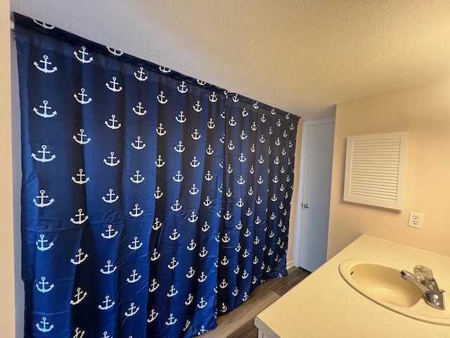 bathroom with a sink, a textured ceiling, a shower with shower curtain, and wood finished floors