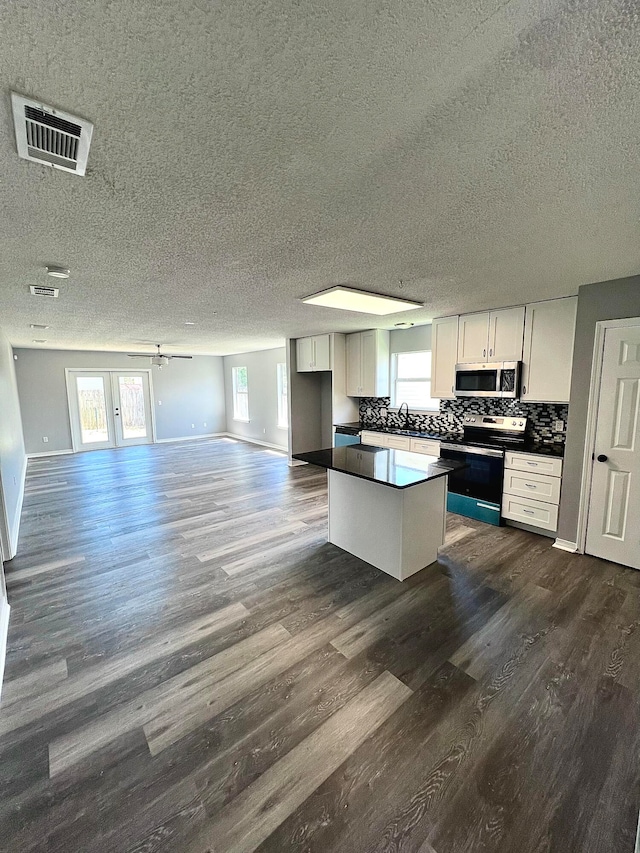 kitchen with a textured ceiling, dark hardwood / wood-style floors, appliances with stainless steel finishes, decorative backsplash, and white cabinetry