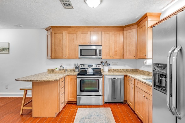 kitchen with a kitchen bar, stainless steel appliances, kitchen peninsula, and light hardwood / wood-style flooring