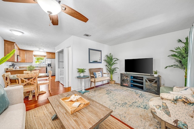 living room with a textured ceiling, ceiling fan, sink, and light wood-type flooring