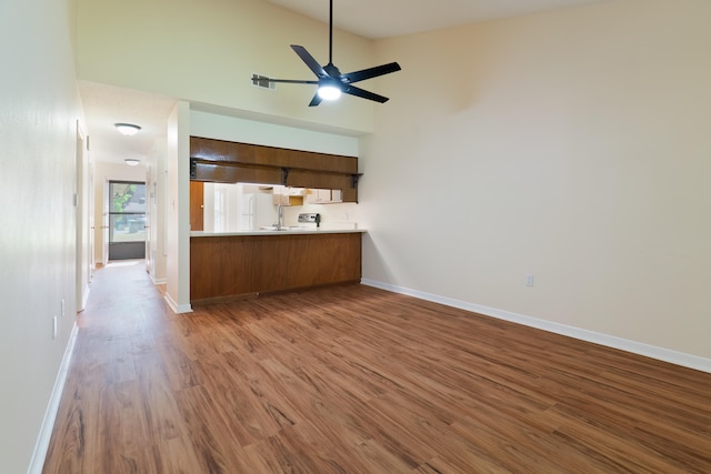 kitchen with high vaulted ceiling, kitchen peninsula, wood-type flooring, and ceiling fan