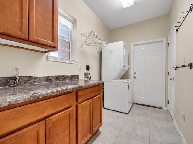 laundry room with light tile patterned flooring, cabinets, and stacked washer / dryer