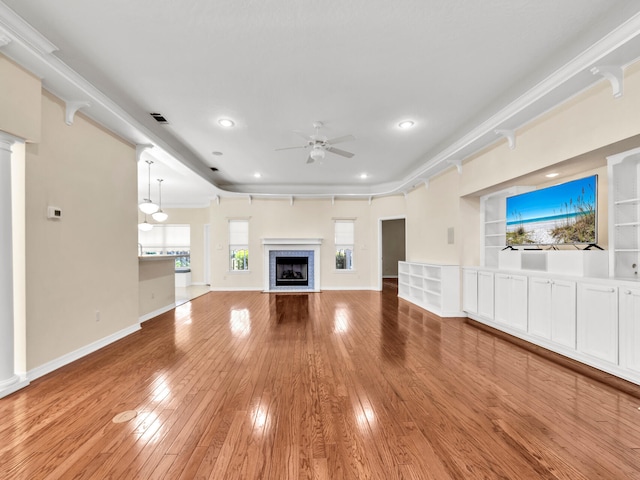 unfurnished living room featuring hardwood / wood-style floors, crown molding, ceiling fan, built in features, and a tiled fireplace