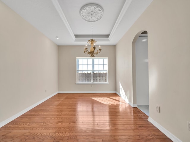 empty room featuring an inviting chandelier, ornamental molding, a tray ceiling, and light hardwood / wood-style flooring