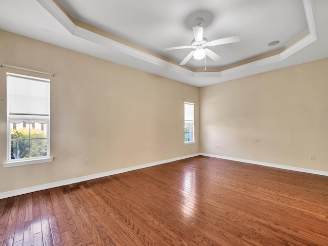 unfurnished room featuring a raised ceiling, ceiling fan, plenty of natural light, and hardwood / wood-style flooring