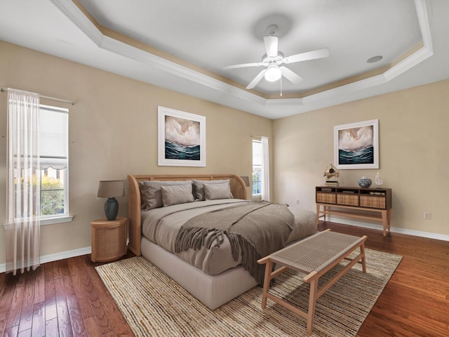 bedroom with hardwood / wood-style flooring, multiple windows, a tray ceiling, and ceiling fan