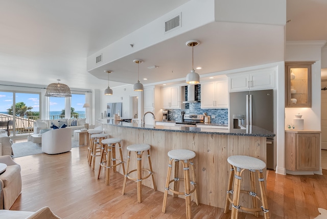 kitchen featuring light wood-type flooring, white cabinetry, hanging light fixtures, appliances with stainless steel finishes, and a breakfast bar area