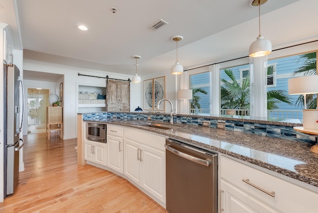 kitchen featuring stainless steel appliances, sink, a barn door, dark stone countertops, and light wood-type flooring