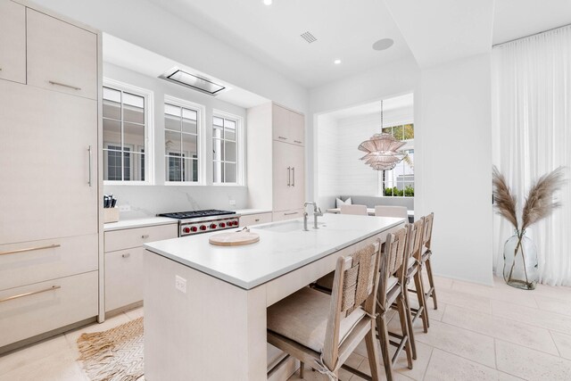 kitchen featuring stainless steel gas stovetop, light tile patterned floors, an island with sink, a kitchen bar, and sink