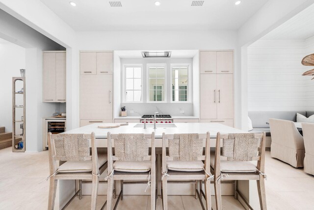 kitchen with beverage cooler, a kitchen bar, an island with sink, and sink