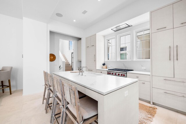 kitchen with stainless steel range, a kitchen breakfast bar, sink, a center island with sink, and white cabinets