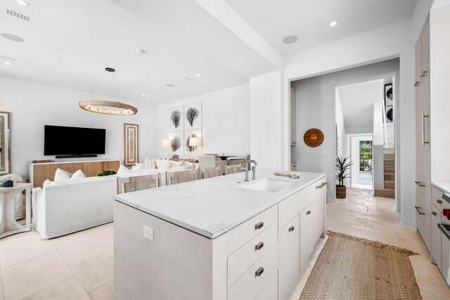 kitchen featuring a kitchen island with sink, white cabinetry, light stone counters, sink, and light tile patterned flooring