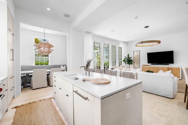 kitchen featuring decorative light fixtures, light tile patterned floors, an island with sink, sink, and white cabinetry