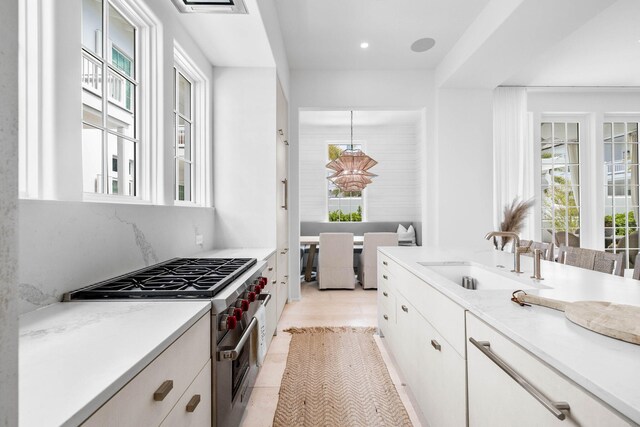 kitchen with decorative light fixtures, light tile patterned floors, sink, white cabinets, and luxury range