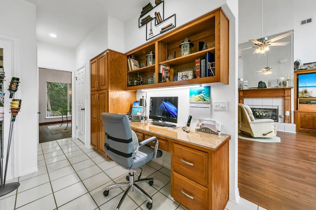 tiled office space with ceiling fan, built in desk, and a tile fireplace