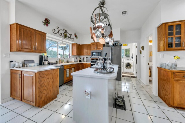 kitchen featuring a center island, light tile patterned floors, appliances with stainless steel finishes, decorative light fixtures, and washer / clothes dryer