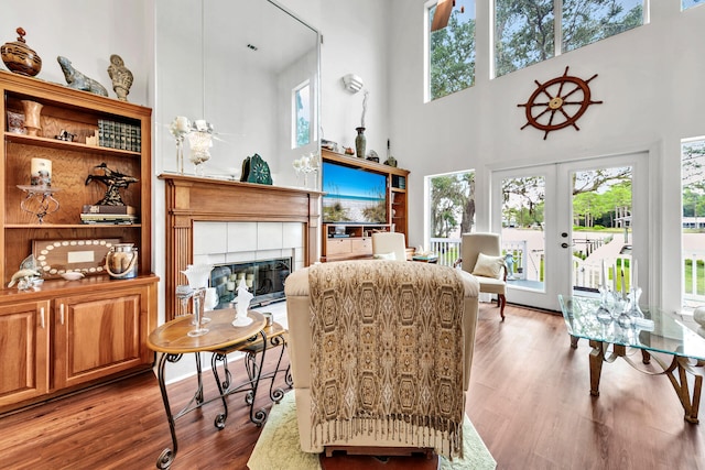 living room featuring a tile fireplace, a healthy amount of sunlight, a towering ceiling, and wood-type flooring