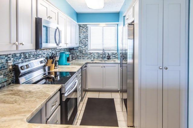 kitchen with stainless steel appliances, a sink, tasteful backsplash, light tile patterned floors, and light stone counters