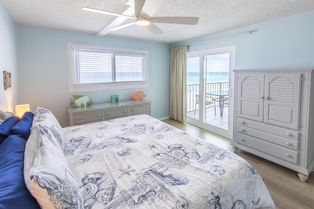 bedroom with access to outside, a textured ceiling, multiple windows, and light wood-type flooring