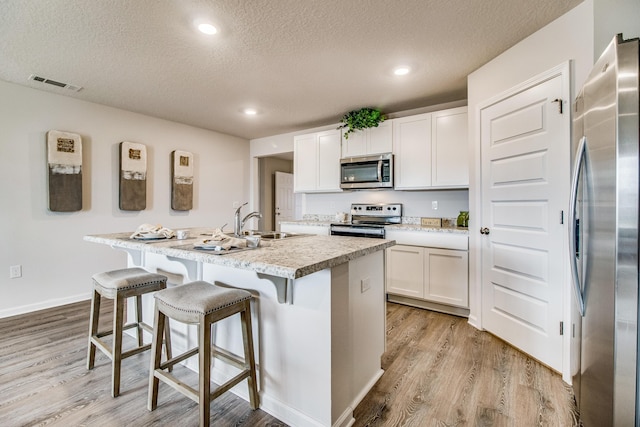 kitchen featuring a kitchen island with sink, visible vents, white cabinets, appliances with stainless steel finishes, and light wood finished floors