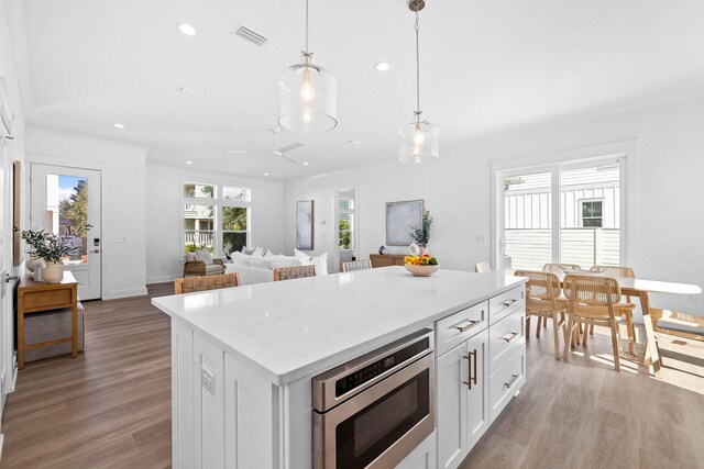 kitchen featuring pendant lighting, white cabinetry, a center island, light stone countertops, and light hardwood / wood-style floors